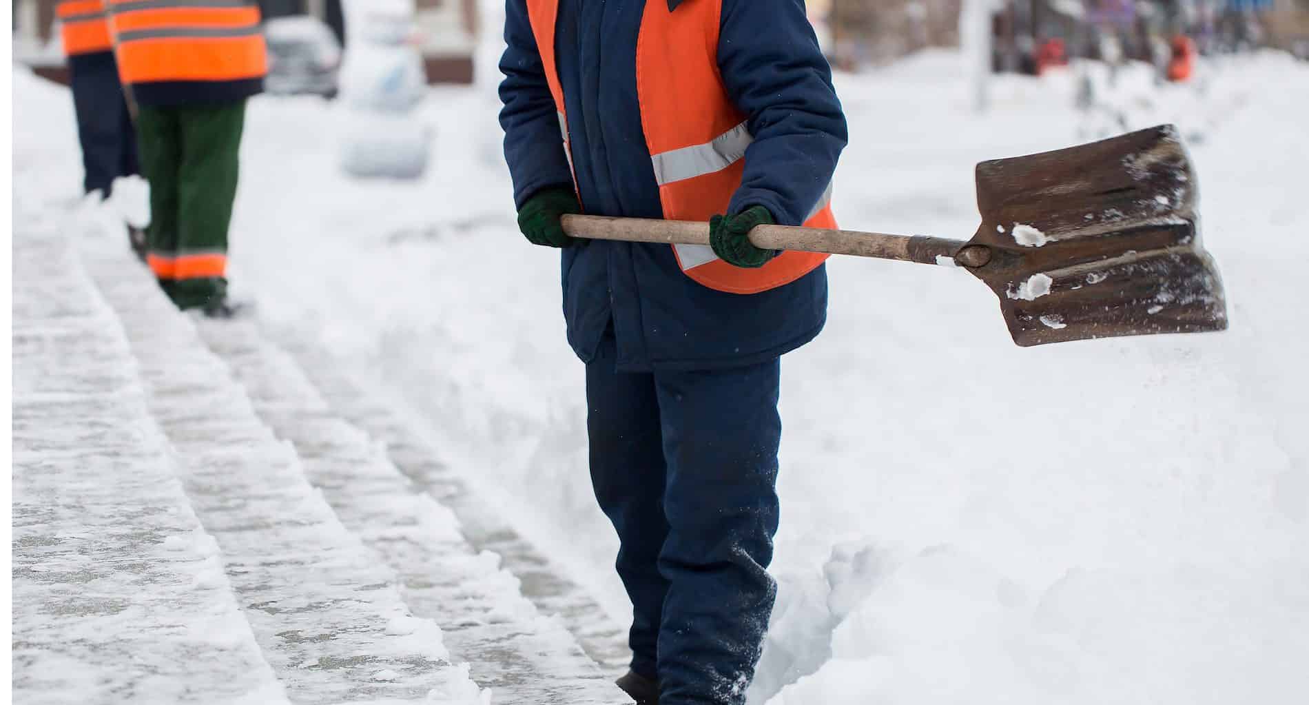 
                     Employees of municipal services in a special form are clearing snow from the sidewalk with a shovel
                     